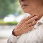 A man touching his throat indicating that he has a swallowing disorder