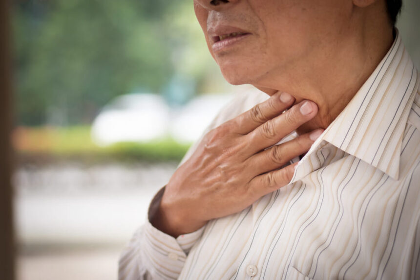 A man touching his throat indicating that he has a swallowing disorder